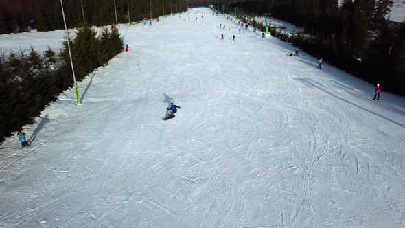 Aerial view of one person snowboarding down slope in Topolita Snow Summit, with drone flying forward alt