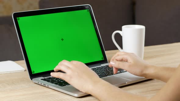 A woman is typing on a laptop with green screen sitting on the working place in an office