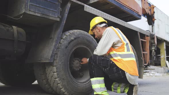 Portrait of Young Mechanic in Work Clothes and Hardhat Checking Construction Vehicles Tires alt