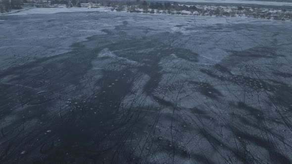 Drone Flight Over a Frozen Lake Where Children Train and Play Hockey Near the Shore on a Cloudy Day