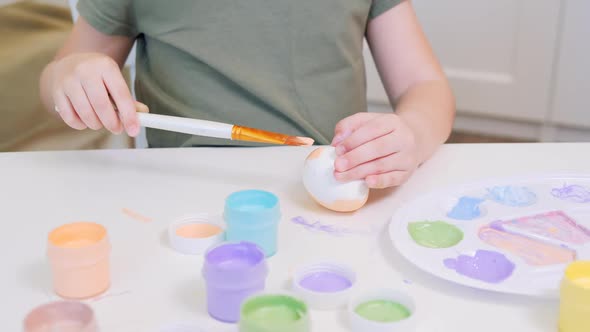 A Small Child Paints a White Chicken Egg in Beige Using a Drawing Bone alt