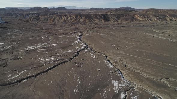 Flying from over top of snow stripped dune towards winding river alt
