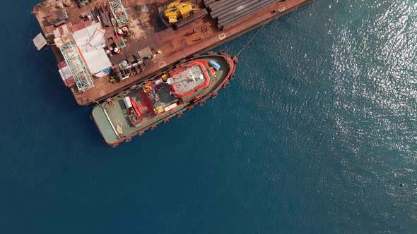 Aerial flyover industrial crane loading pipes on old rusted ship during sunny day at Gili Trawangan alt
