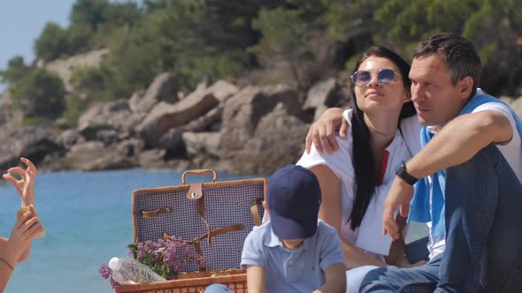Family picnic with boy and girl near sea on sunny summer day. Basket with water, fruit and croissant alt