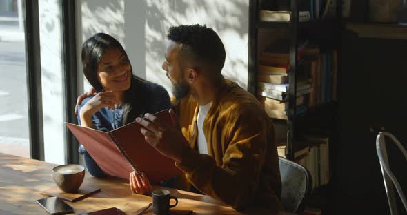 Front view of young mixed-race couple discussing over menu card in cafe 4k alt