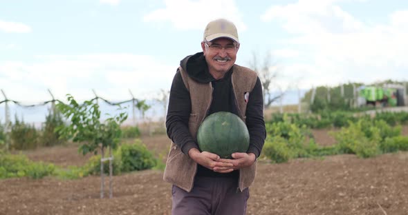 Portrait of a happy smiling farmer in an agricultural field with a ripe watermelon in his hands alt