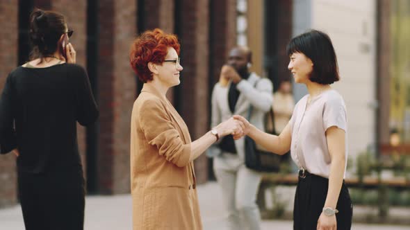 Two Businesswomen Shaking Hands and Talking on Street alt