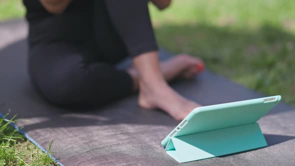 Closeup Tablet on Exercise Mat with Unrecognizable Senior Sportswoman Training Sitting at Background alt