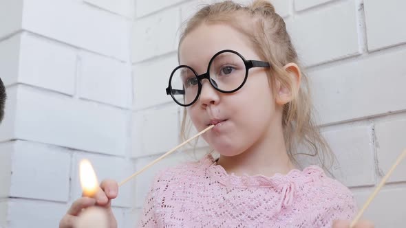 A Teenage Girl in Big Round Glasses Eats a Fried Marshmallow on a Stick in the Company of Her