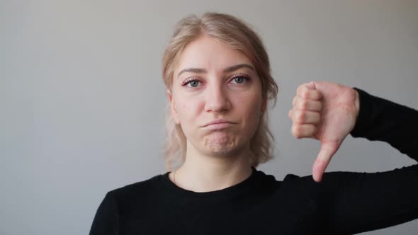 Portrait of young woman expressing discontent and showing thumb down