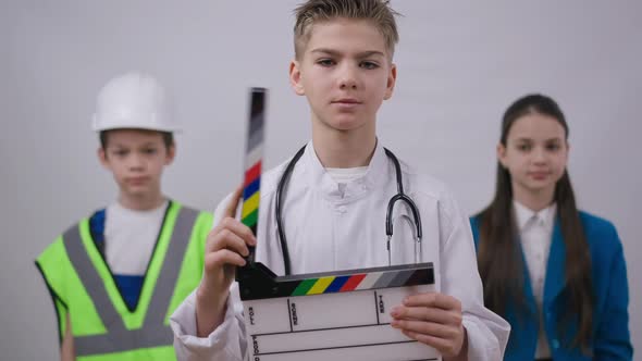 Smiling Boy in Medical Gown Posing with Clapper Board As Friends Builder and Photographer Crossing alt