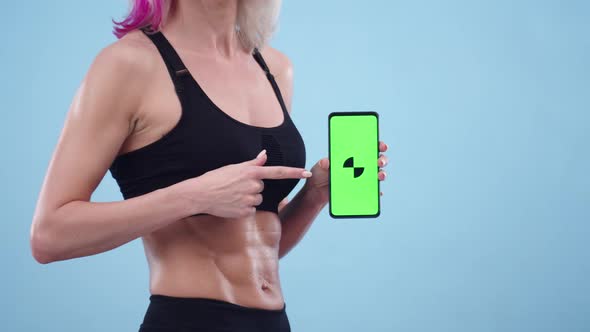 Woman in Sports Top and with a Muscular Stomach Holds a Phone with an App Closeup alt