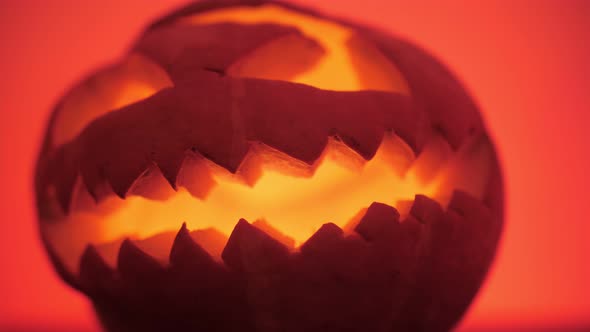 sinister Halloween pumpkin with burning candles inside, red background alt