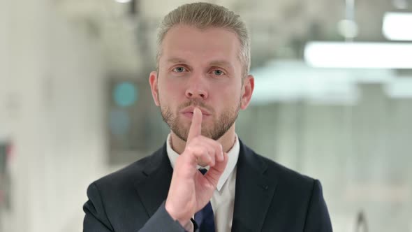 Portrait of Serious Businessman Putting Finger on Lips  alt