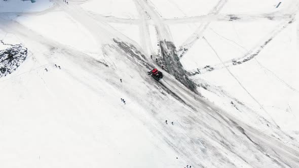 Aerial View Red Modern Snowcat Ratrack Descends From the Slopes of the Mountain Along a Rolled Road alt