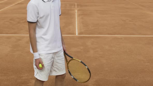 Male athlete in sportswear holding racket and tennis ball, training on court alt