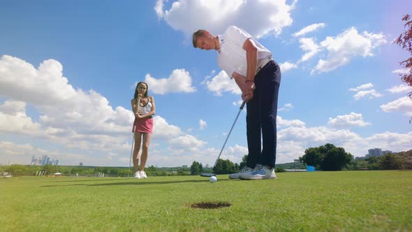 The Ball Is Falling Into the Hole with a Man and a Woman Looking at It alt