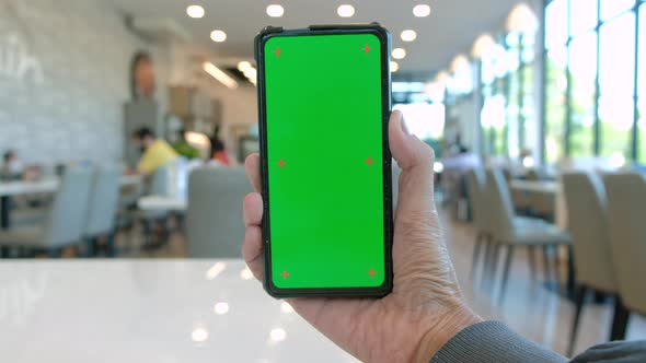 Asian man's hand holding a mobile phone with chroma key green screen display at a coffee shop