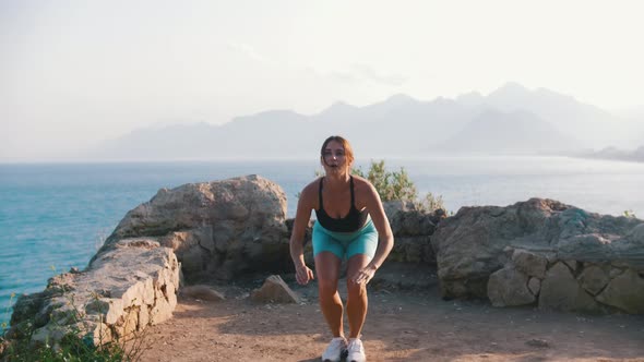 Sportive Woman Doing Fitness Outdoors By the Sea  Squatting and Jumping alt