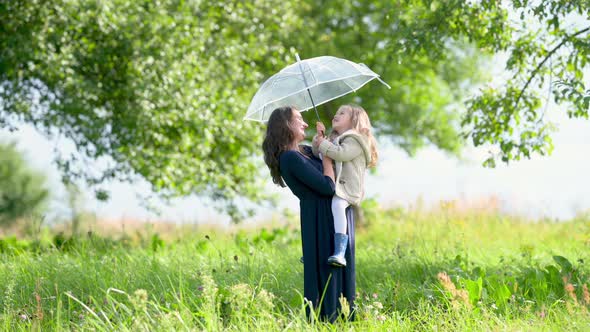 Young mother with her little daughter in a park holding an umbrella.