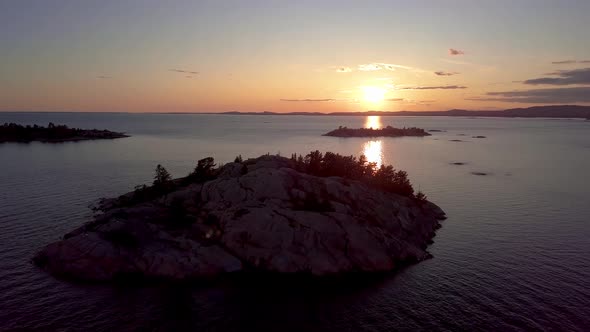 Rocky Island with Pine Trees in Blue Lake at Sunset, Drone Aerial Wide Orbit Pan Pedestal Down. Flyi alt