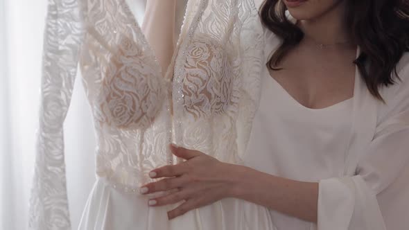 Bride in Lingerie Standing with Her Wedding Dress at Home Near Window White Boudoir Dress and Veil alt