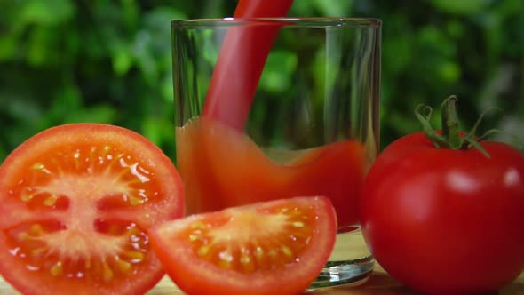 Closeup of Tomato Juice Poured in a Glass Next to Tomato Cut Into Halves alt
