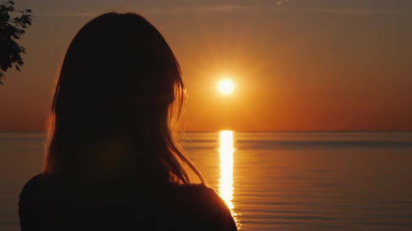 Silhouette of a Middle-aged Woman Who Watches the Sunset Over the Sea alt