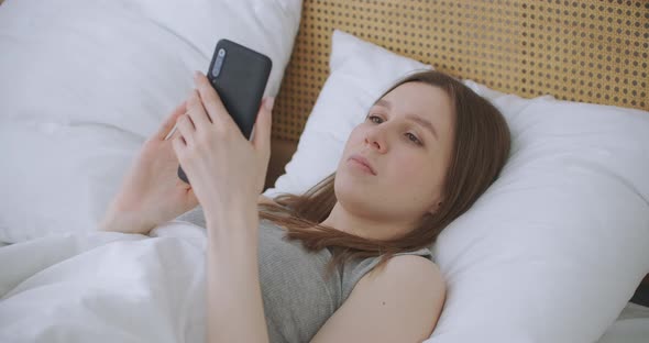 Woman in Morning Sitting in Bedroom Leaning Against the Soft Leather Back of Bed. Write Messages alt