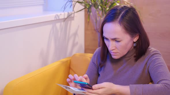 a Woman is Sitting in a Yellow Armchair and Typing on a Smartphone alt