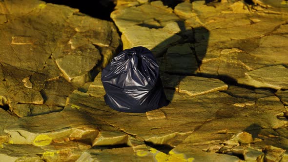 Black Trash Bag Lay on a Rocky Beach alt