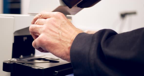 A college professor setting up a slide of cells under a microscope to show his students in a biology alt