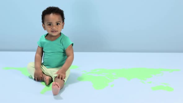 Baby boy sitting on world map on floor alt