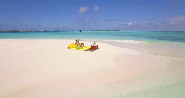 Aerial drone view of a man and woman couple having a picnic meal on a tropical island beach alt