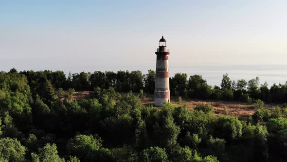 Old lighthouse at open space of small island, green bushes around, aerial shot