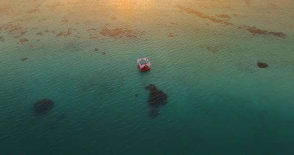Aerial drone view of a man and woman having dinner on a floating raft boat at sunset alt