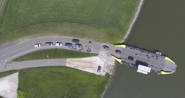 A topdown drone shot of a ferry, loading off cars en people from a river to land, tripod shot, in th alt
