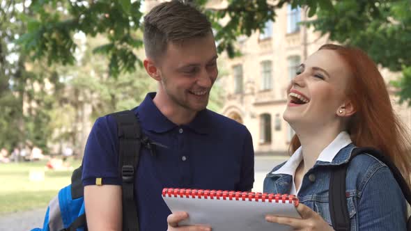 Female Student Asks Her Classmate About Something in Notebook on Campus alt