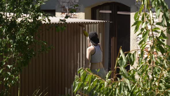 girl in a cap paints a garage with a roller outside alt