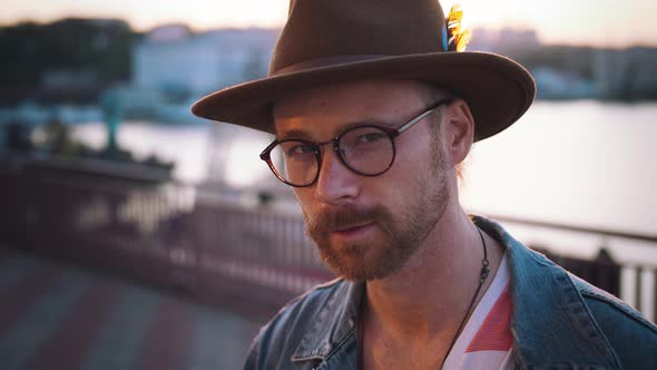 Colorful Portrait of Young Stylish Guy with Red Beard in Glasses and in Hat Looking at Camera During alt