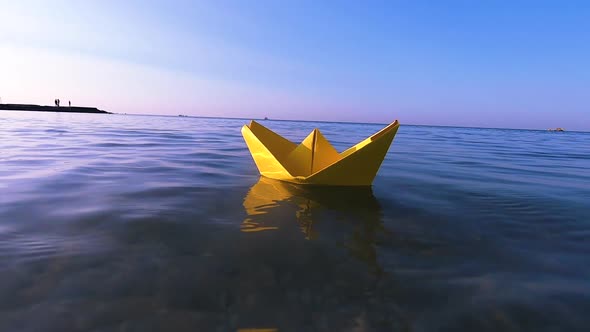 Yellow Paper Boat Floats on Surface of Blue Water Waves of Sea Closeup alt