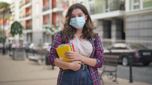 Portrait of Smart Charming College Student in Coronavirus Face Mask Posing on City Street with Books alt