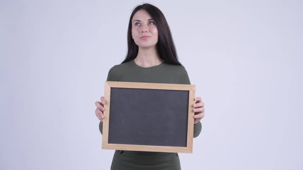 Happy Young Beautiful Woman Thinking While Holding Blackboard alt