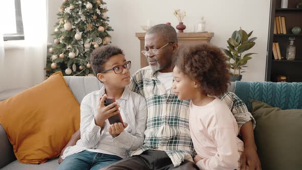 Carefree African American Boy and Girl Resting on Sofa with Grandfather and Web Surfing in Internet alt