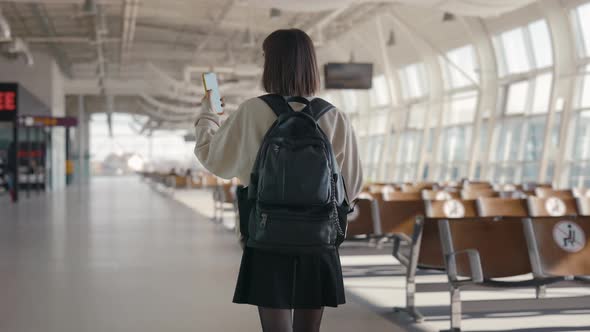 Female Tourist Using Cell Phone While Walking at Airport alt