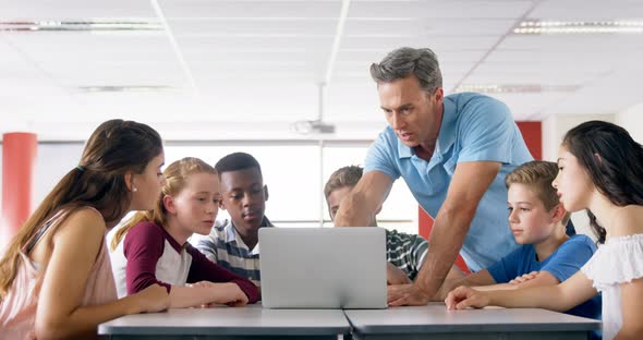 Teacher assisting schoolkids on laptop 4k alt
