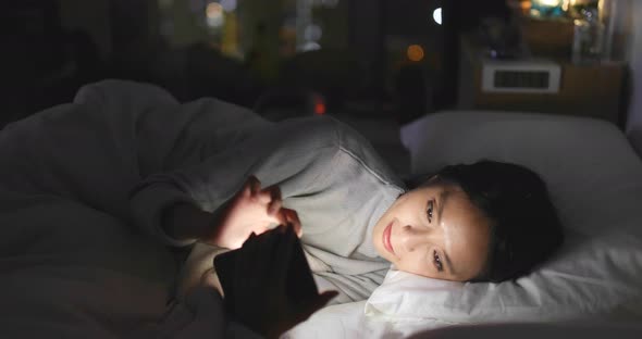 Woman using cellphone and lying on bed at night alt