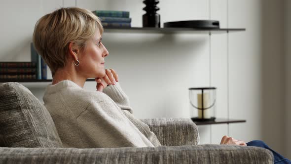 A Middleaged Woman is Sitting Alone in an Armchair and Looking at the View From the Window alt