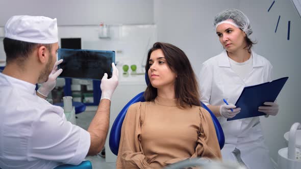 Male Dentist Analyzing Xray Talking with Female Patient at Clinic alt