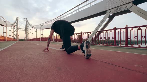 Young Man in Black Sports Uniform Runs on the Pedestrian Bridge at Dawn alt
